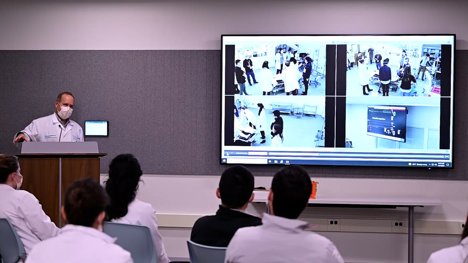 Simulation Center classroom with a man at a podium in front of a screen with students.