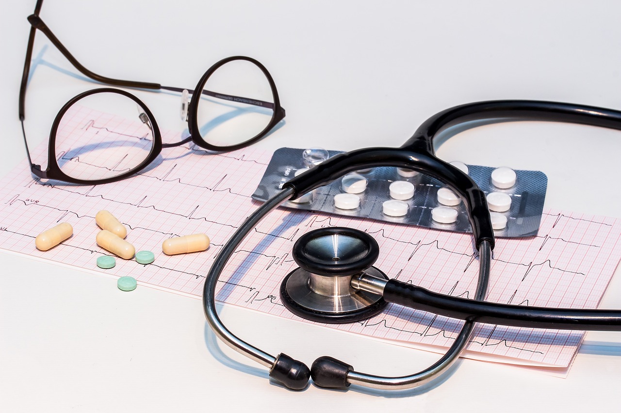 Pair of glasses, stethoscope, and medication tabs on top of heart monitor graph