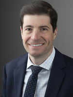 Professional headshot of a man wearing a navy blue suit, light blue shirt and black tie with gold polka dots.