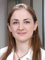 Woman with brown hair wearing a white shirt and necklace.