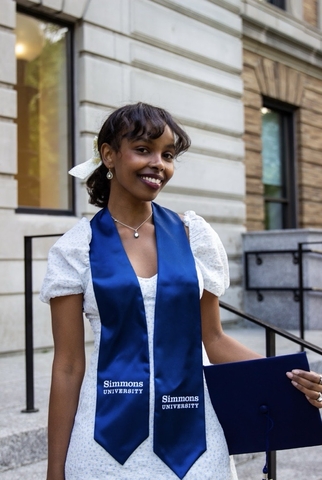 A young woman in a white dress holds a blue diploma while smiling.