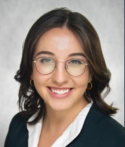 Woman in glasses, smiling, wearing black suit jacket and white shirt.