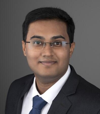 Manish smiling in front of a grey background