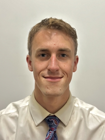 Man with short hair wearing a white shirt and blue tie with white dots.