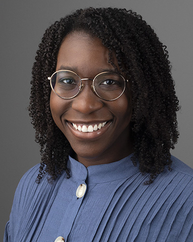A woman with glasses and curly hair smiling with teeth showing.