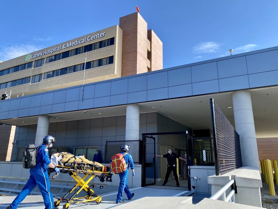 Two med flight workers in blue suits wheel a stretcher into Lahey hospital