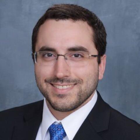 Tony in a black suit smiling in front of a blue background