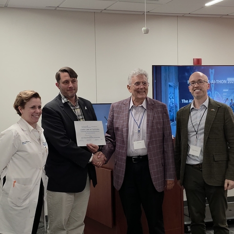 Four people standing in a room with a certificate being handed to the person in the white coat