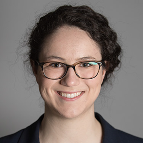 A smiling woman with glasses, wearing a white shirt and a navy blazer.