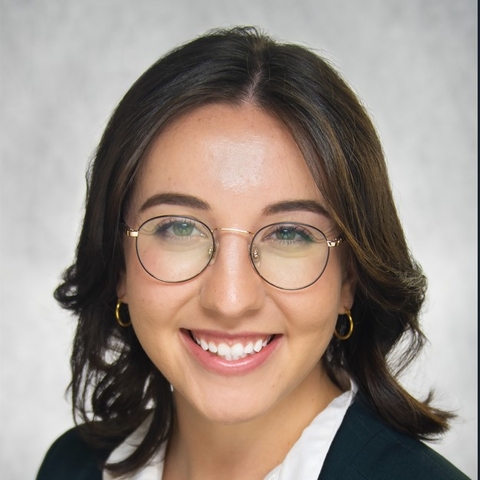 Woman in glasses, smiling, wearing black suit jacket and white shirt.