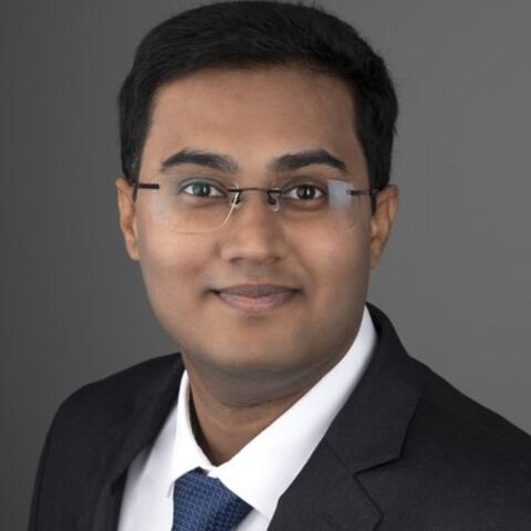 Manish smiling in front of a grey background