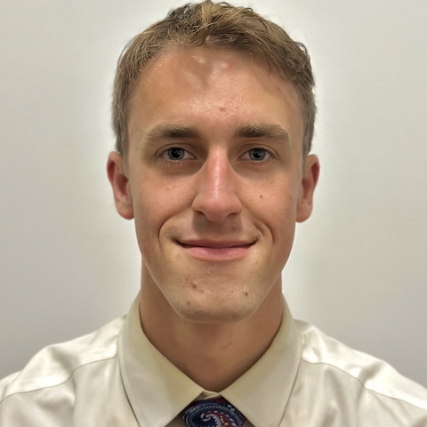 Man with short hair wearing a white shirt and blue tie with white dots.