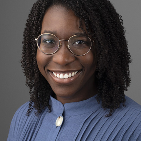 A woman with glasses and curly hair smiling with teeth showing.