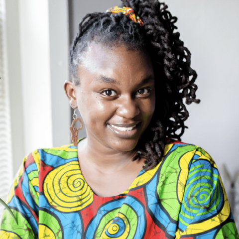 African woman with curly hair wearing colorful patterned shirt, smiling.