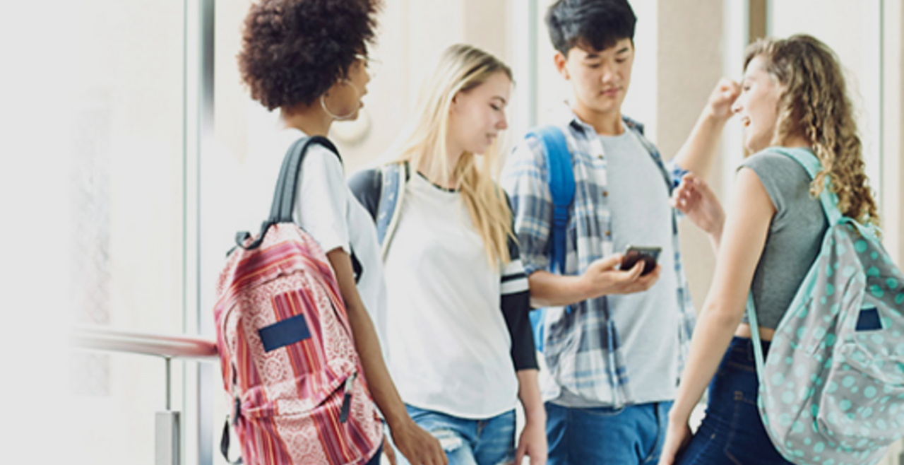Group of four teenagers with backpacks talking amongst themselves