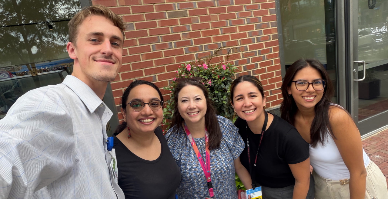 Five people smiling at a conference in front of a brick building.
