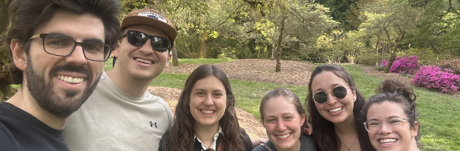 Six people smiling in a park with trees and plants in the background.