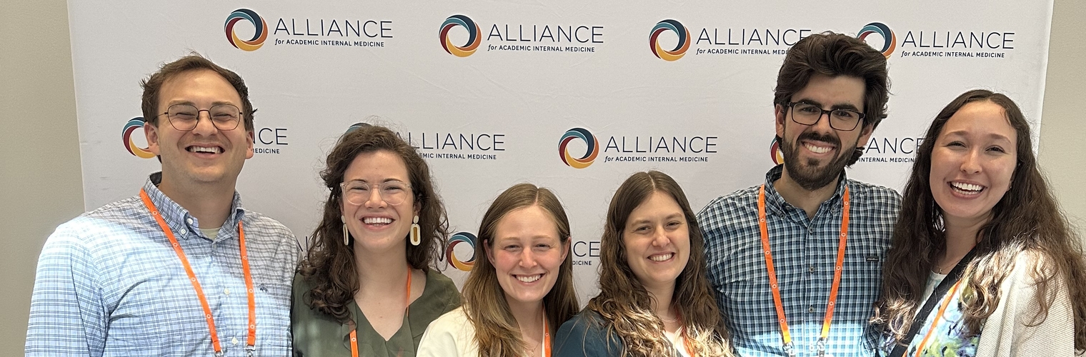 Six people standing in front of a banner with the word Alliance for Academic Internal Medicine.