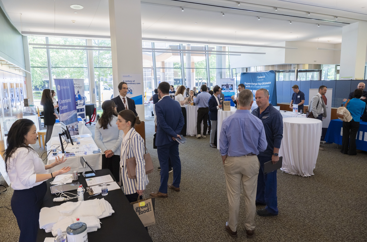 Several people interact at a conference with tables and booths in a modern, well-lit room.
