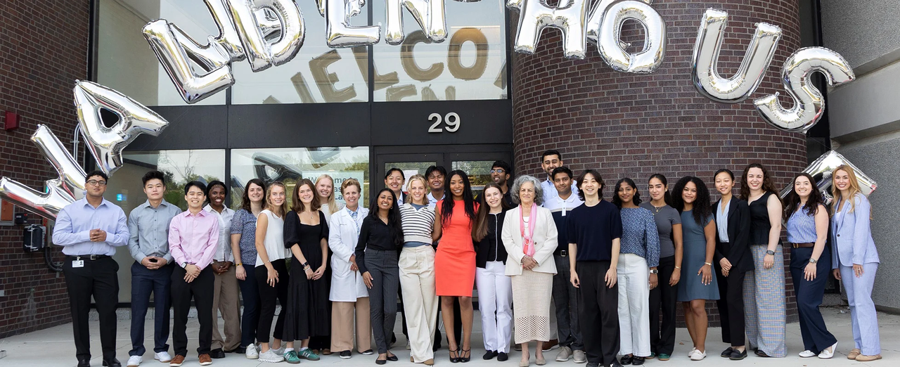 A group of people in formal attire stand in front of a building with "Landen House US" in balloons above.