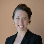 Dr. Tess Wiskel in a black blazer, bun hairstyle, and earrings smiling at camera.