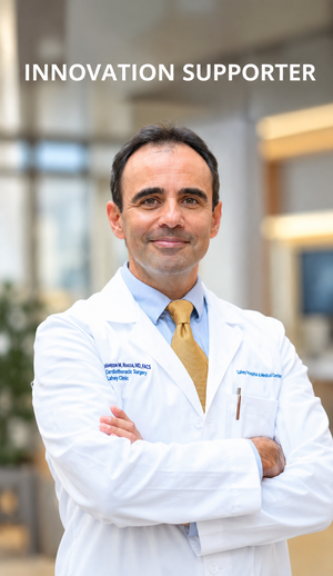 A smiling man in a white lab coat and yellow tie with his arms folded.