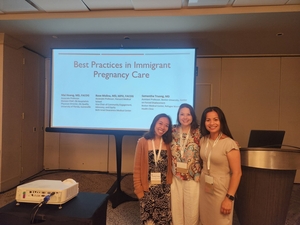 Three women stand in front of a presentation on immigrant pregnancy care.
