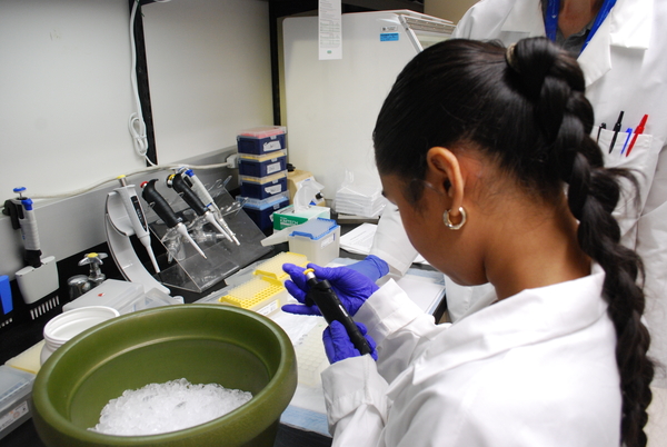 Woman in lab coat holding pipette over a bowl of ice.