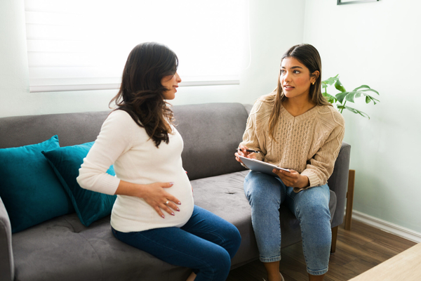 Pregnant woman talking to a doctor while holding her belly.